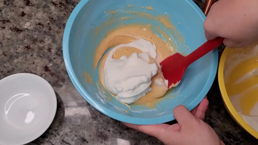 Pouring stiffly beaten egg Into batter with spatula