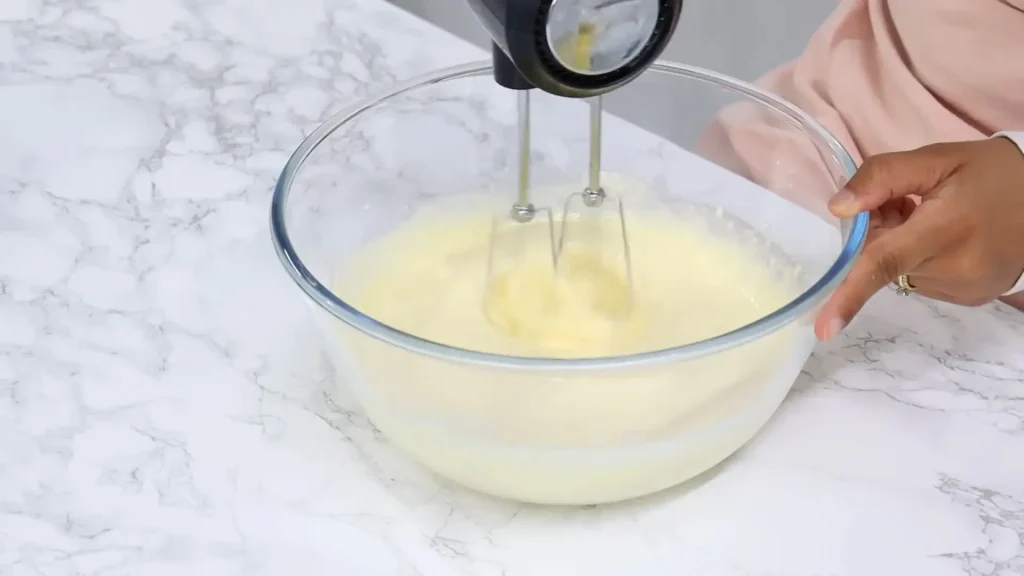 Whisking whipped cream, vanilla extract, and powdered sugar in a bowl with stand mixer 