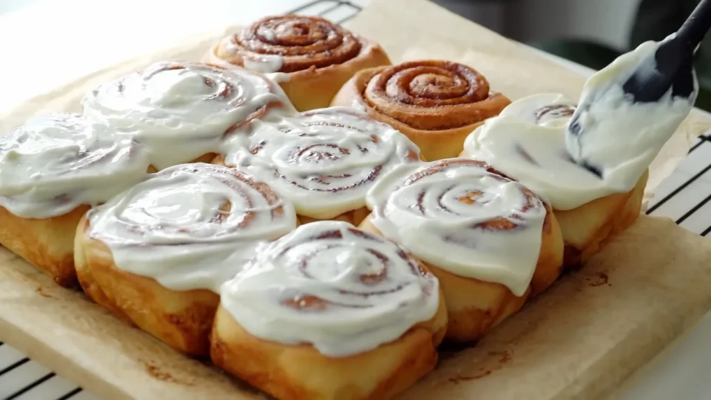 Spreading cheese cream over backed cinnamon rolls with spatula